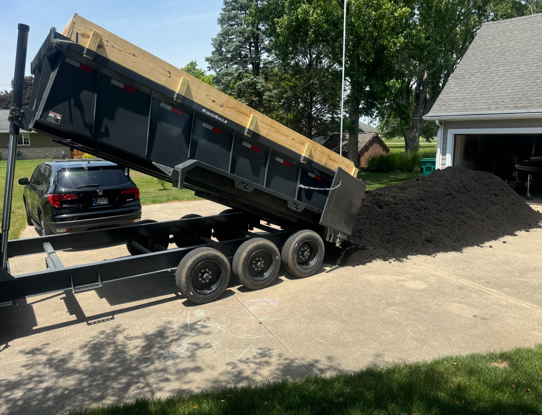 Dump truck unloading asphalt onto a driveway. Black truck, dark asphalt.