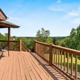 Wooden deck with railing overlooking a green landscape under a blue sky