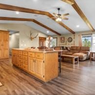 Spacious rustic living room with wood beams, hardwood floors, kitchen island, sofa, and ceiling fan
