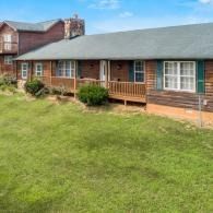 Single-story log cabin with green roof, front porch, and large grassy yard