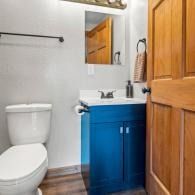 Small bathroom with white toilet, blue vanity sink, wood cabinet, and mirror by a shower area