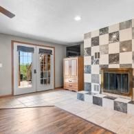 Empty living room with tiled fireplace, hardwood floor, French doors, and a wooden cabinet