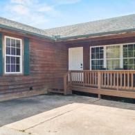 Wooden house exterior with front porch, white door, and large windows under a shingled roof