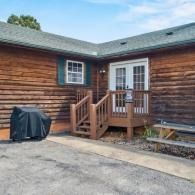 Wood-sided house back entrance with small wooden steps, white door, grill, and paved driveway