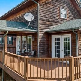 Wooden house deck with railing, sliding glass doors, and a satellite dish under a sloped roof