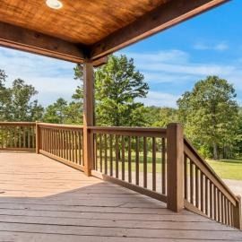 Wooden deck with railings and stairs overlooking a green landscape under a blue sky.
