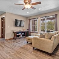 Bright living room with beige sectional, wall-mounted TV, ceiling fan, and large windows
