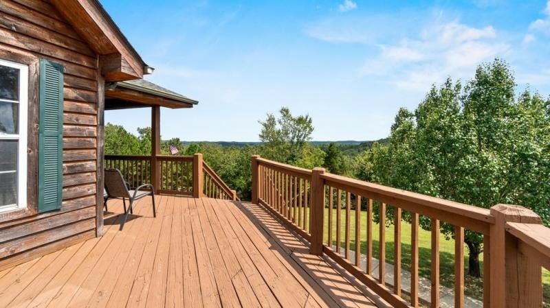 Wooden cabin deck with railing overlooking green trees under a blue sky