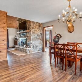 Dining room with wooden table, chandelier, and stone fireplace opening into a bright kitchen