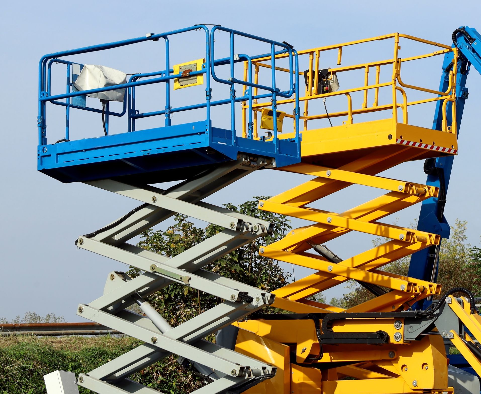 A blue and yellow scissor lift with a cage on top of it