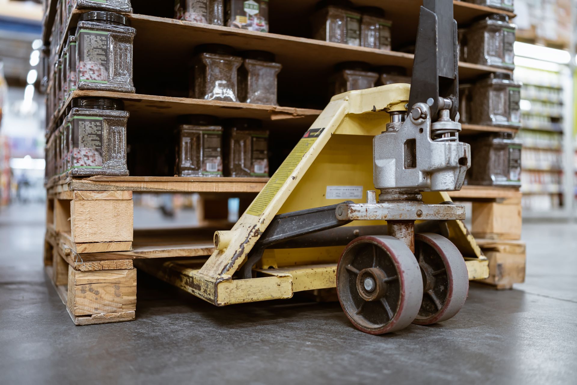 A yellow hand truck is moving a wooden pallet in a warehouse.