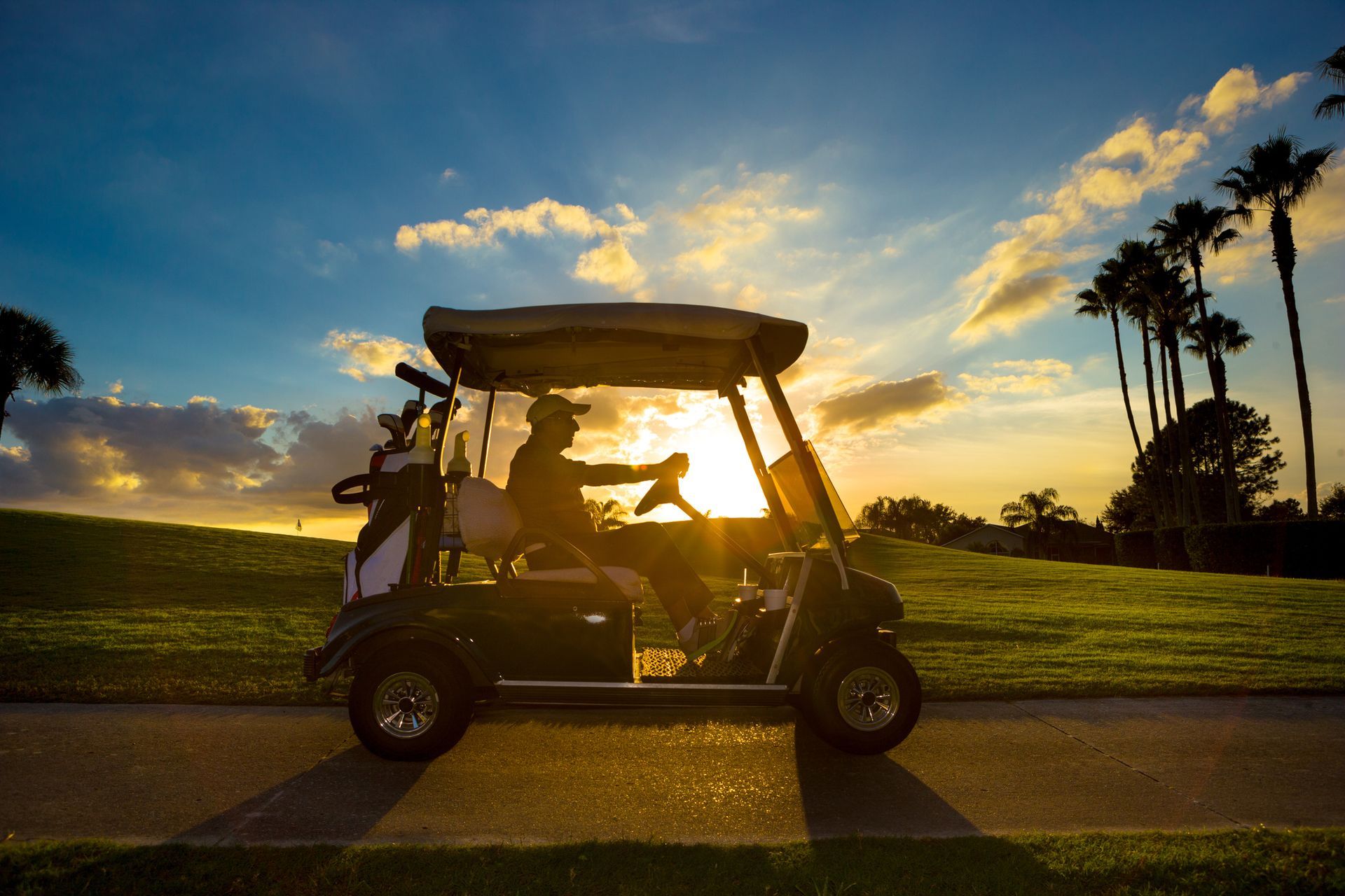 A man is driving a golf cart on a golf course at sunset.