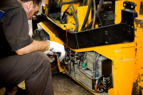 A man is working on a yellow forklift in a garage.