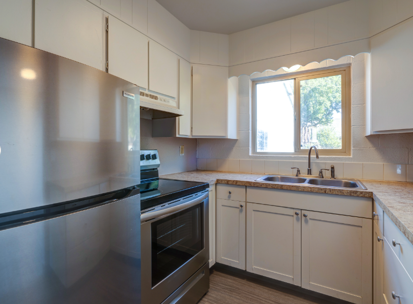 A kitchen with white cabinets , a stove , a sink , and a refrigerator.