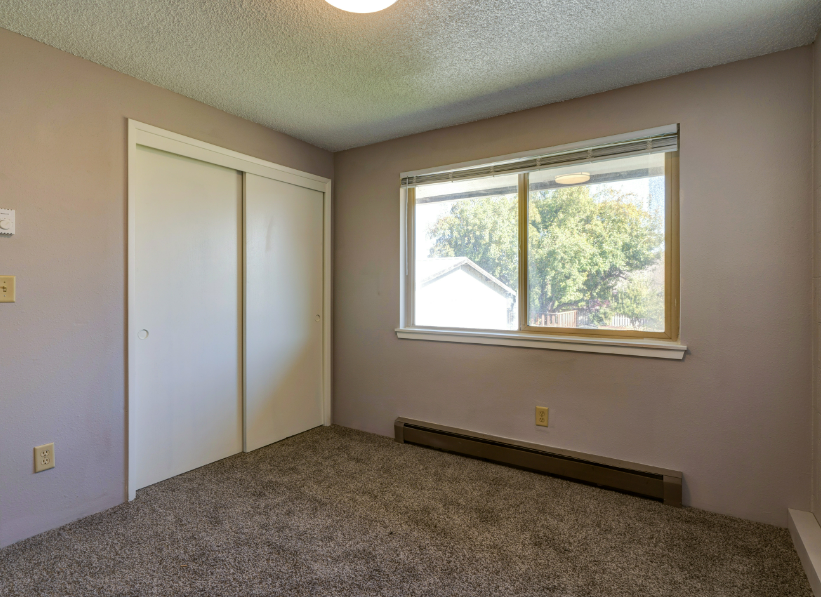 An empty bedroom with a large window and a closet.