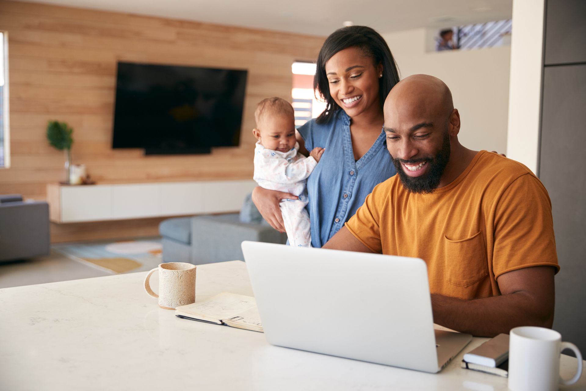 A man and woman are holding a baby while using a laptop computer.