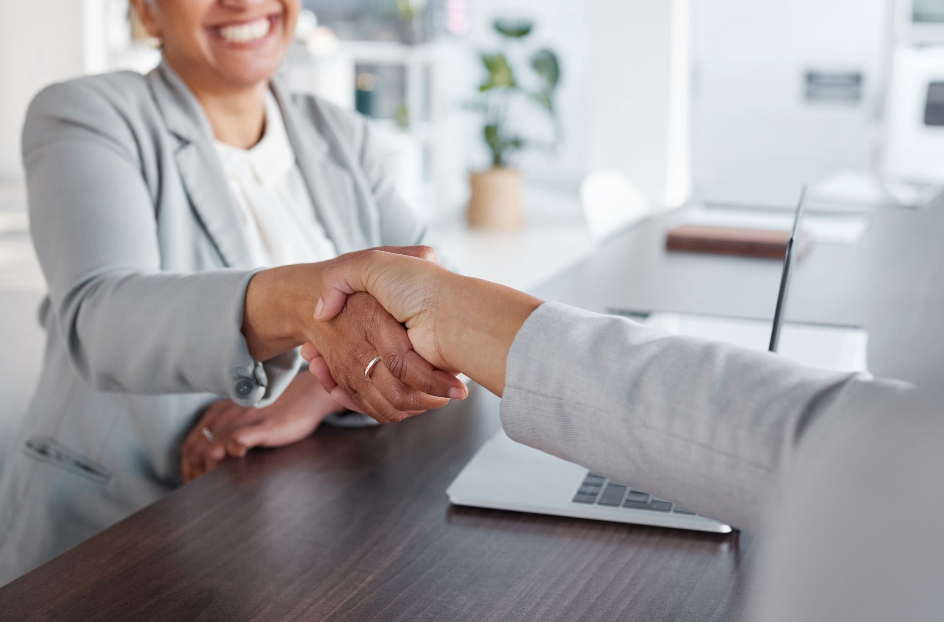 A woman is shaking hands with another woman while sitting at a desk.