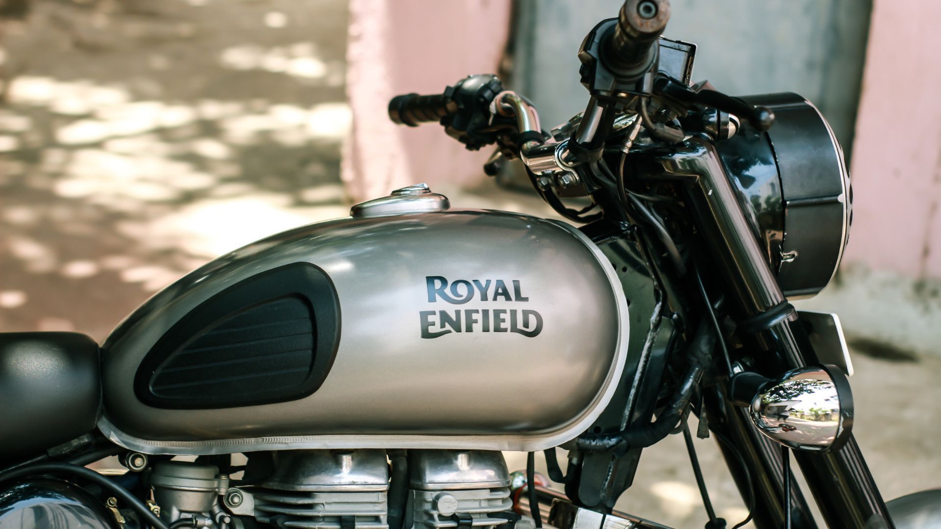 Two black vintage motorcycles parked side by side on cobblestone in front of a brick wall