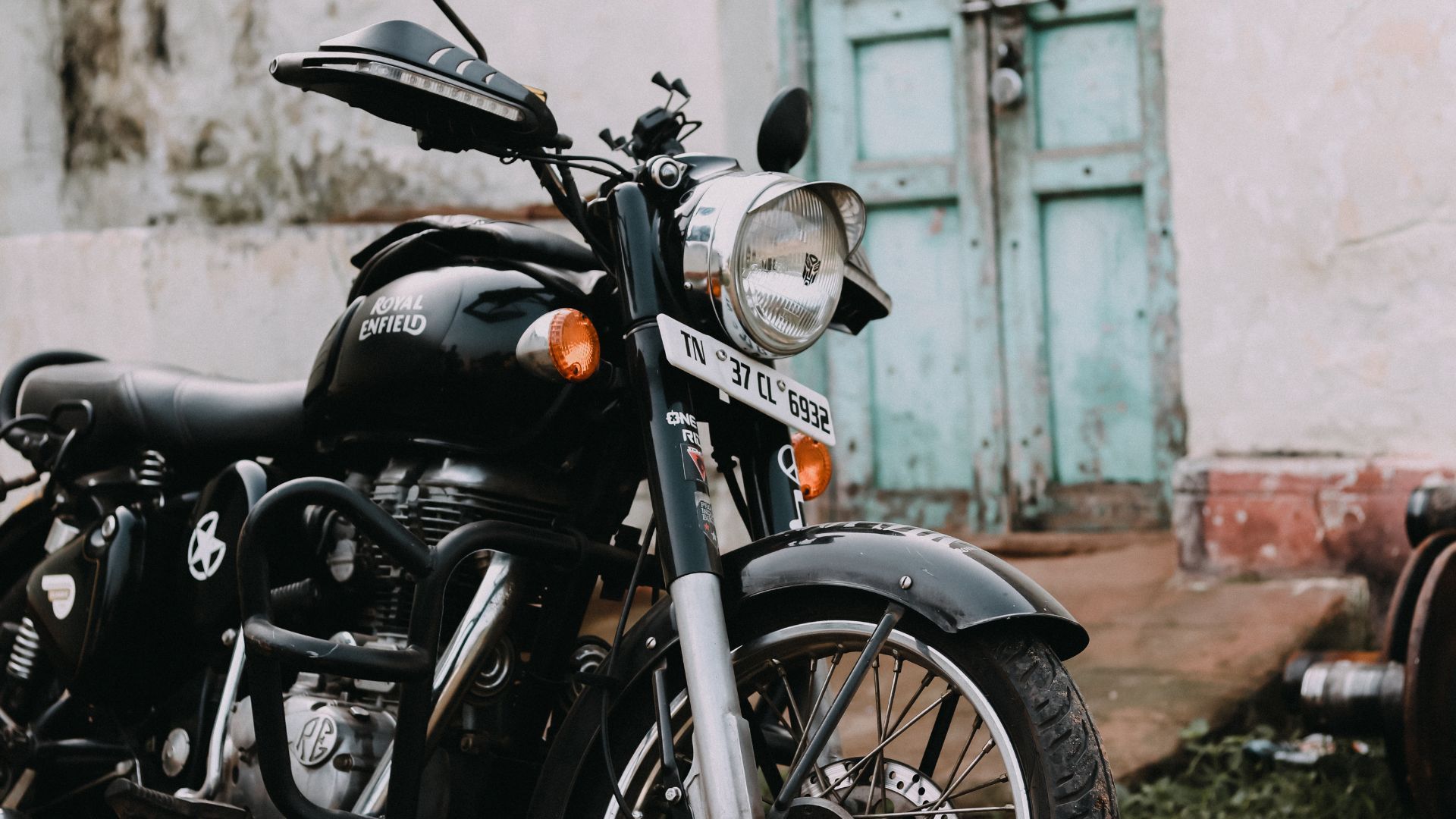 Black motorcycle parked in front of a weathered white wall and turquoise door