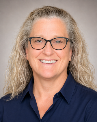 Portrait of a smiling person with gray hair and glasses, wearing a navy shirt