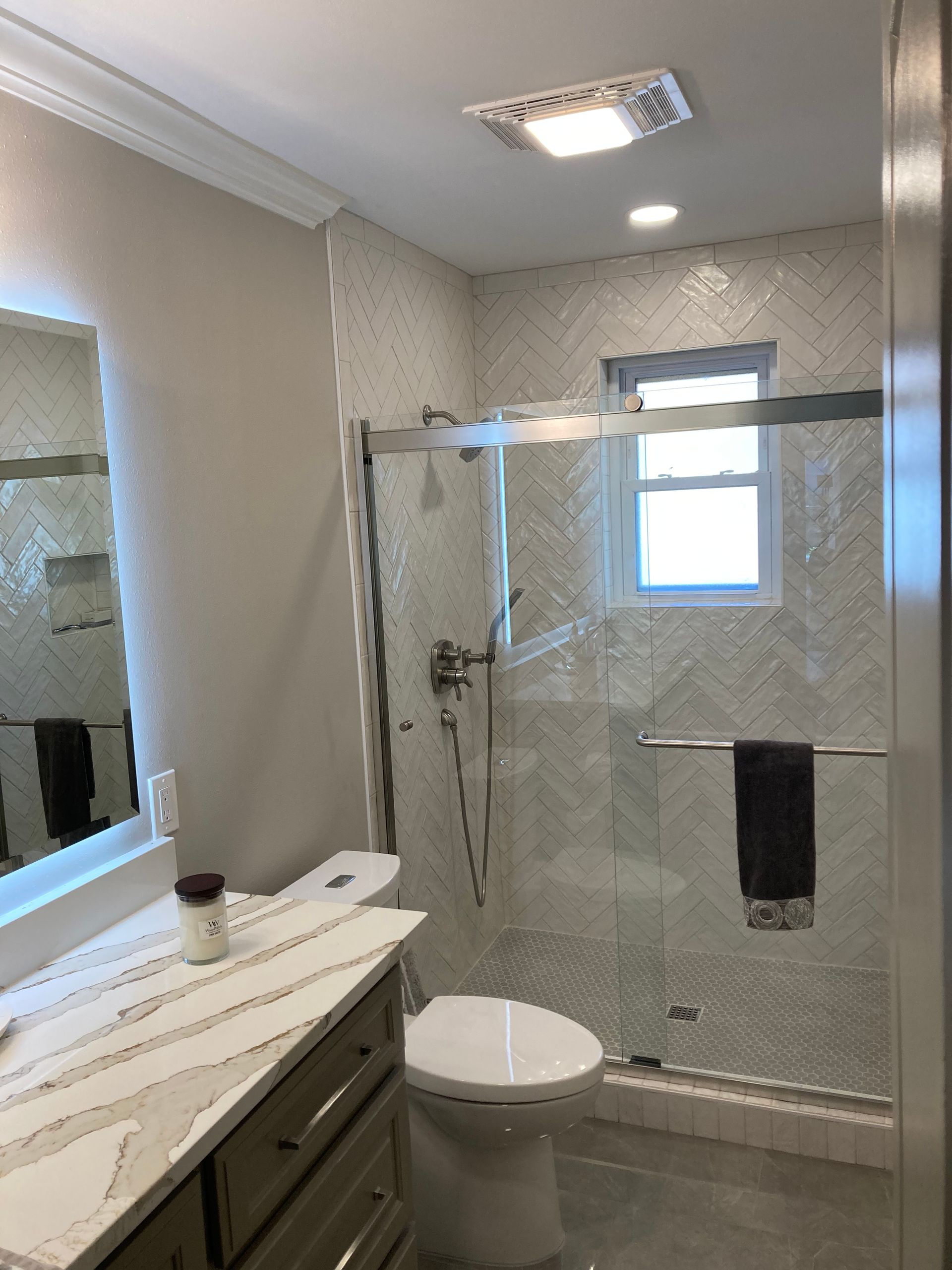 A bathroom with a gray vanity, white herringbone-tiled shower, glass door, and a white toilet.
