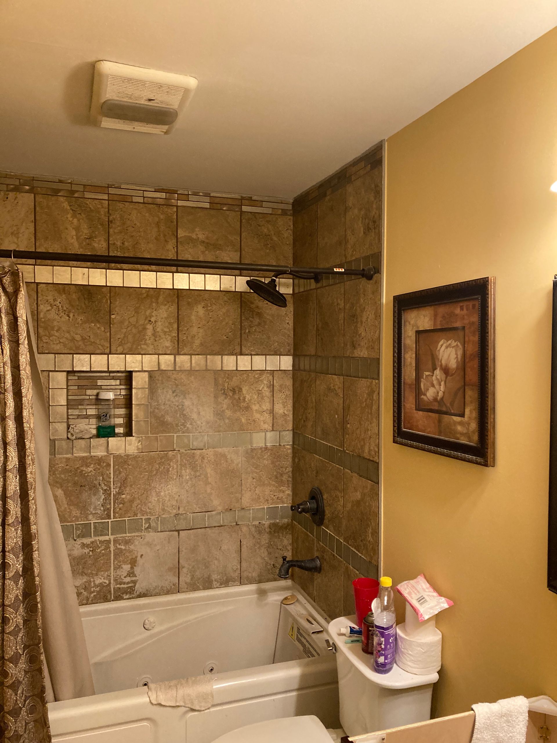 A tiled bathtub and shower alcove next to a toilet, featuring brown walls and a decorative framed picture on the side.
