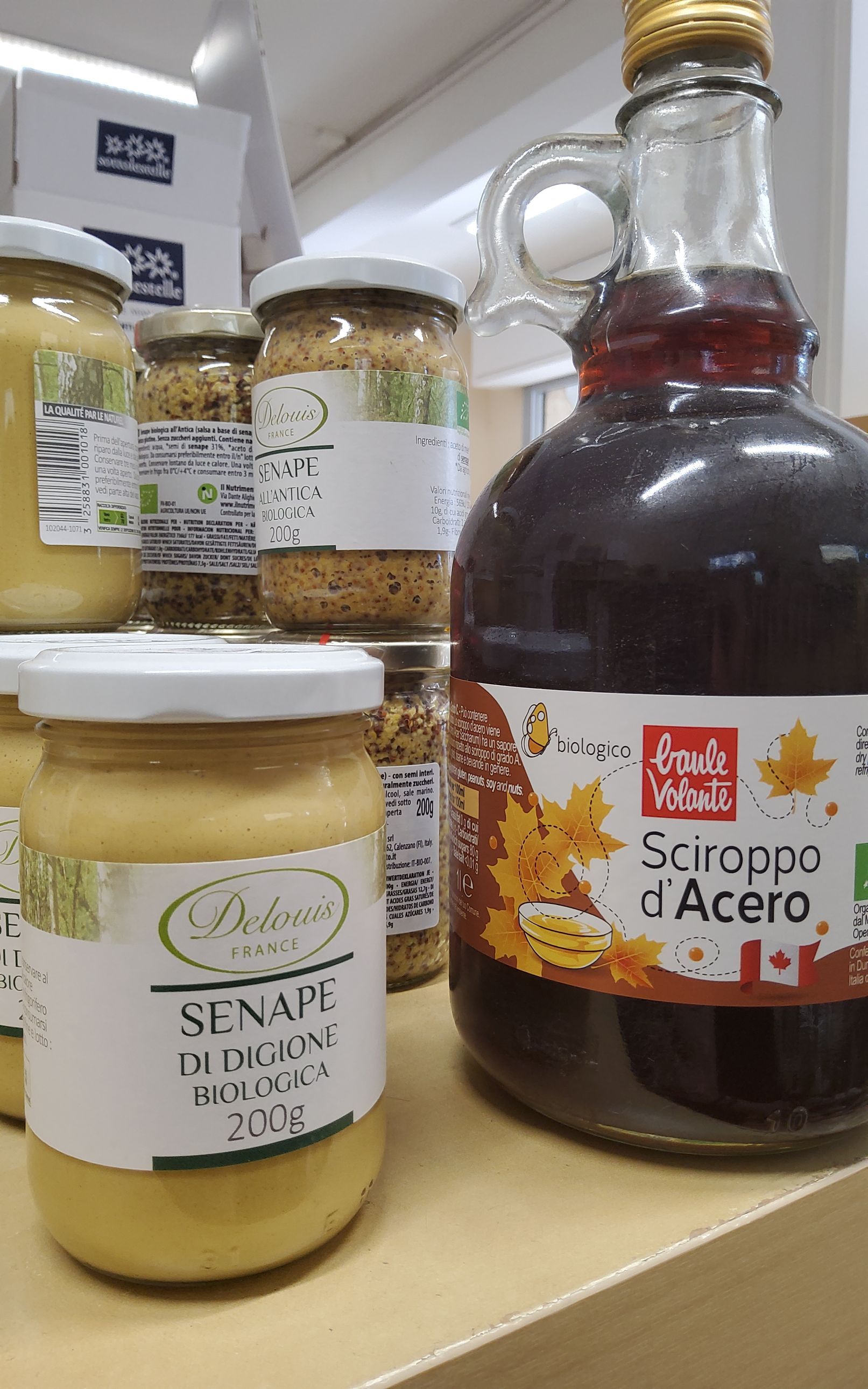 Un barattolo di senape e una bottiglia di sciroppo sono su un tavolo.