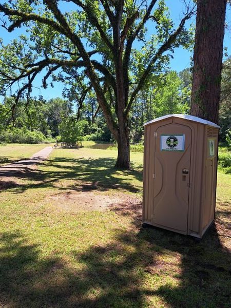 A portable toilet is sitting under a tree in a park