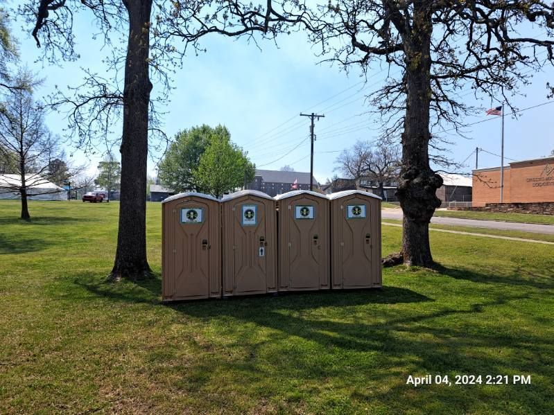 A row of portable toilets are lined up in a grassy field.