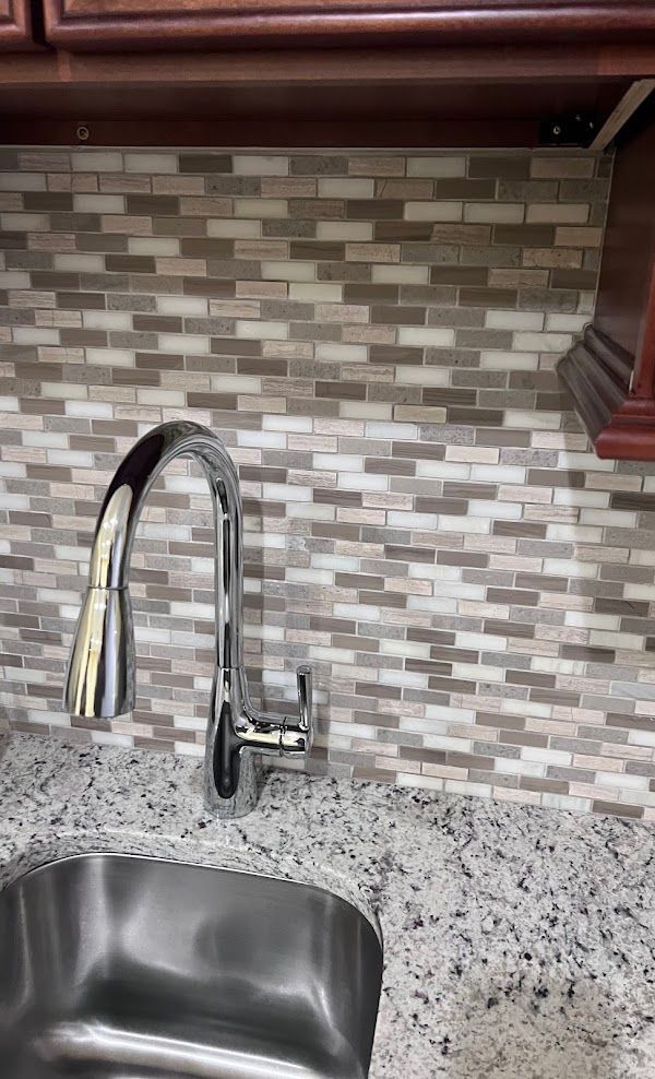 A kitchen sink with a faucet and tile backsplash.