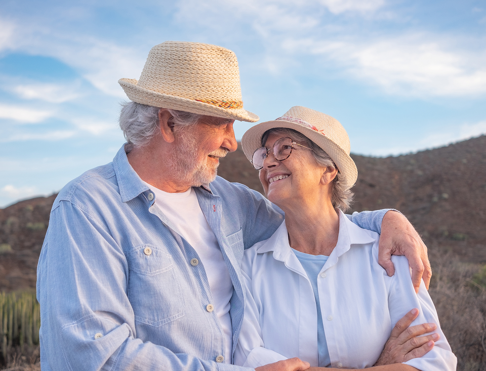 A man and a woman are standing next to each other and smiling . the man is wearing a hat.