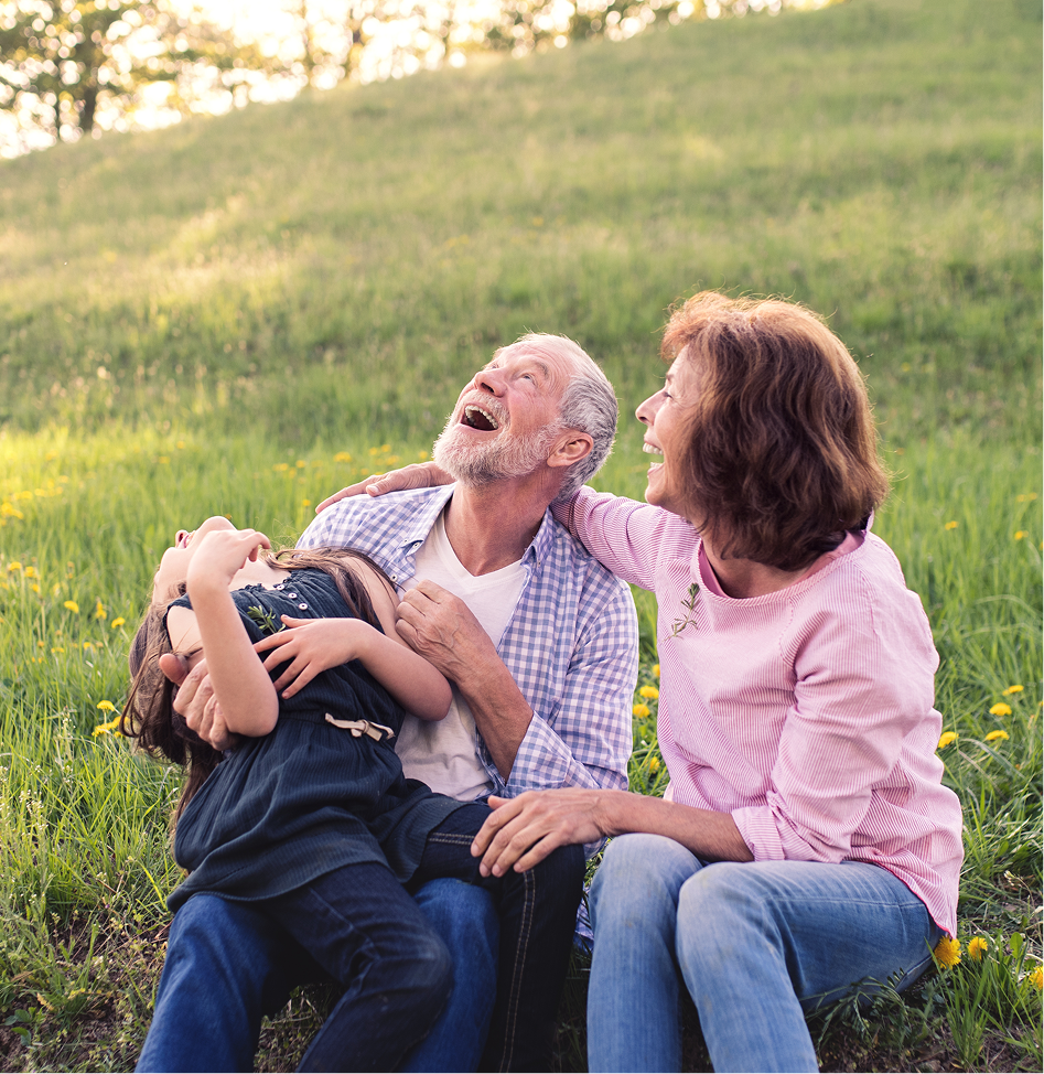 A family is sitting on a blanket on the beach holding hands.