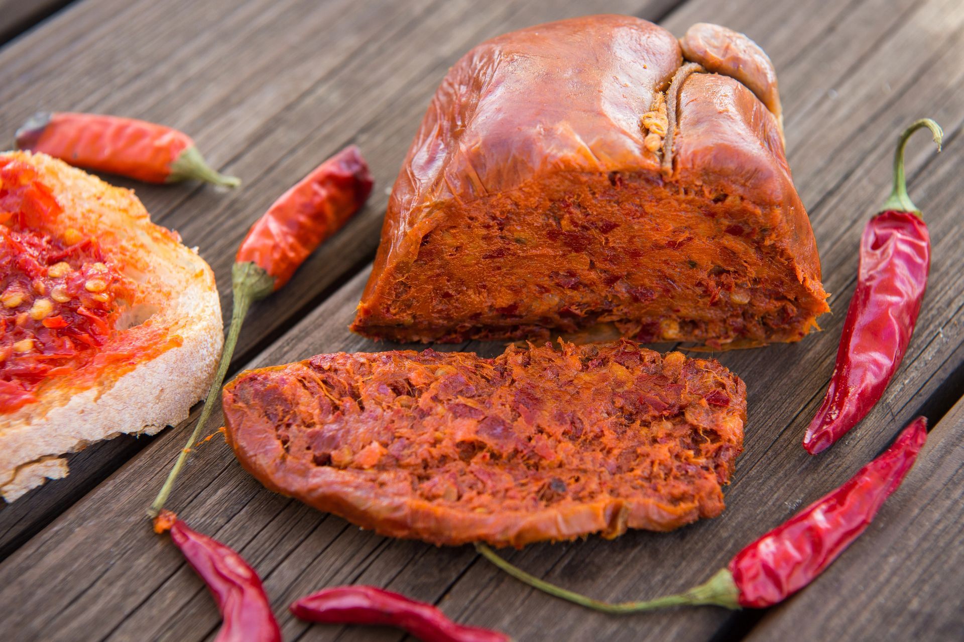 Pasta di peperoncino rosso calabrese e peperoni su una superficie di legno, con una fetta di pane tostato spalmata sulla pasta.