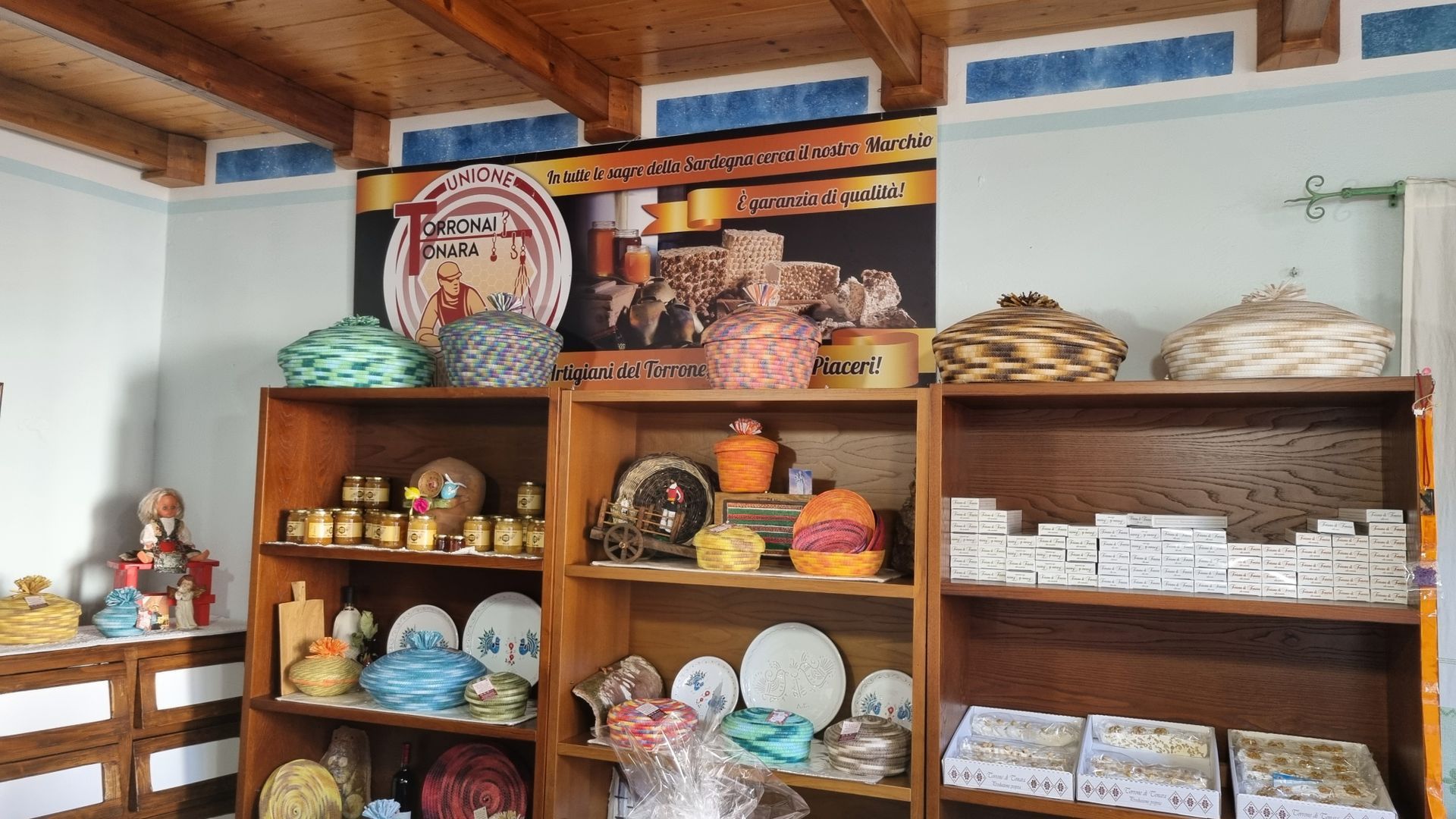 Scaffali pieni di vari articoli artigianali, tra cui cestini e oggetti decorativi, sotto un cartello.