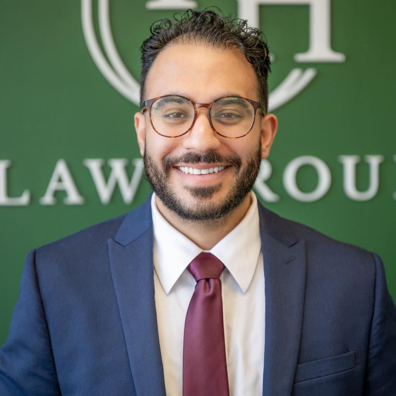 A man in a suit and tie is smiling in front of a law group sign