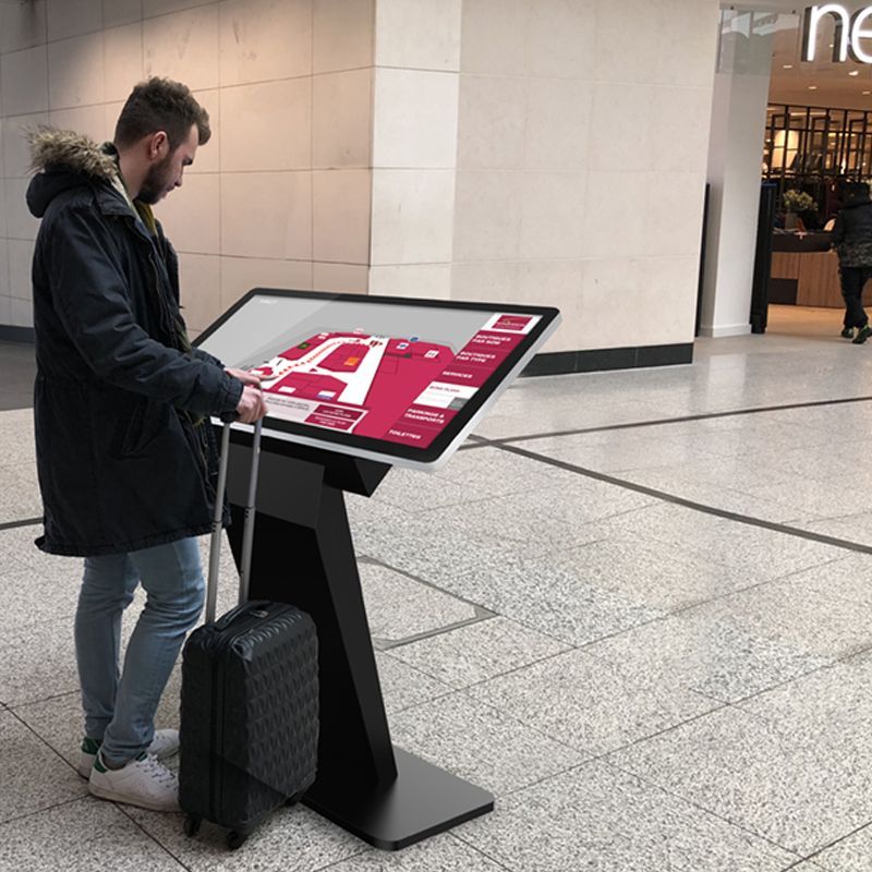 A man with a suitcase is looking at a large screen