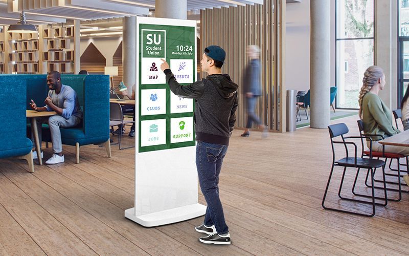 Man using a digital kiosk in a modern library. The kiosk displays various apps and information.