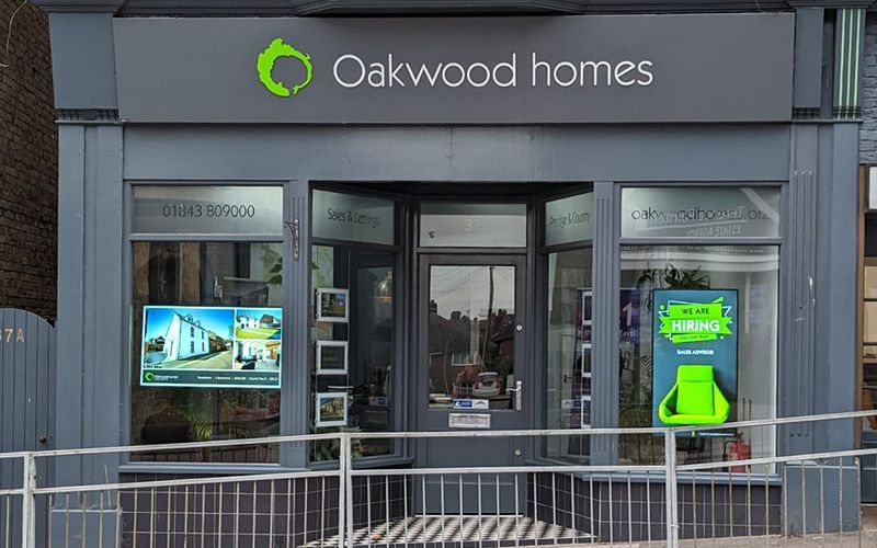 Oakwood Homes real estate office storefront; grey exterior, open doors, signage, display windows.