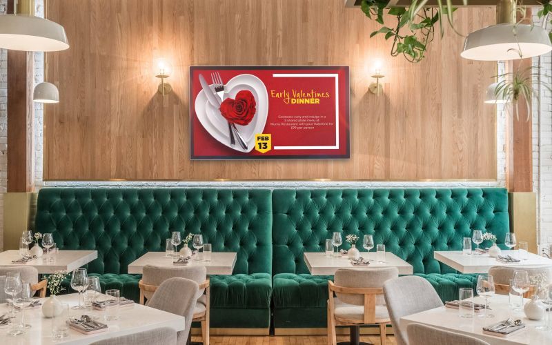 Restaurant interior with green velvet seating, white tables, and a Valentine's Day advertisement.