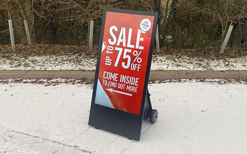 Black A-frame sign on snowy ground, advertising a 75% off sale.