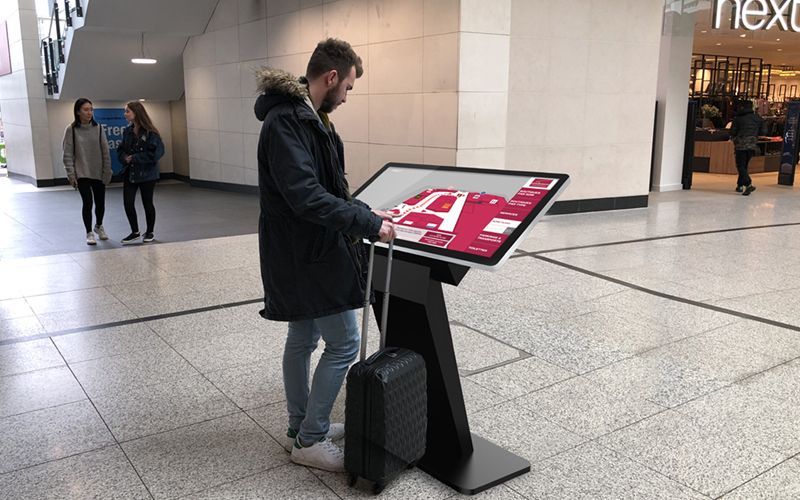 Man using interactive mall directory kiosk, holding luggage.