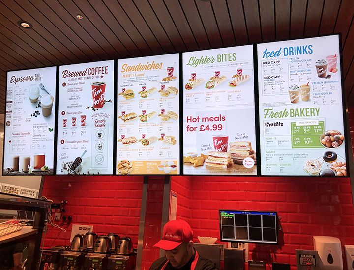 A man in a red hat is behind a counter in a fast food restaurant.