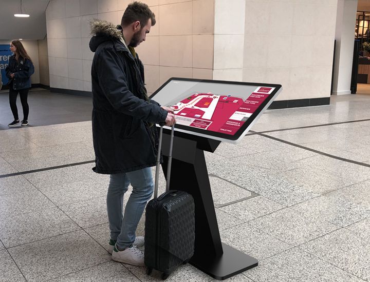 A man with a suitcase is standing in front of a large screen.