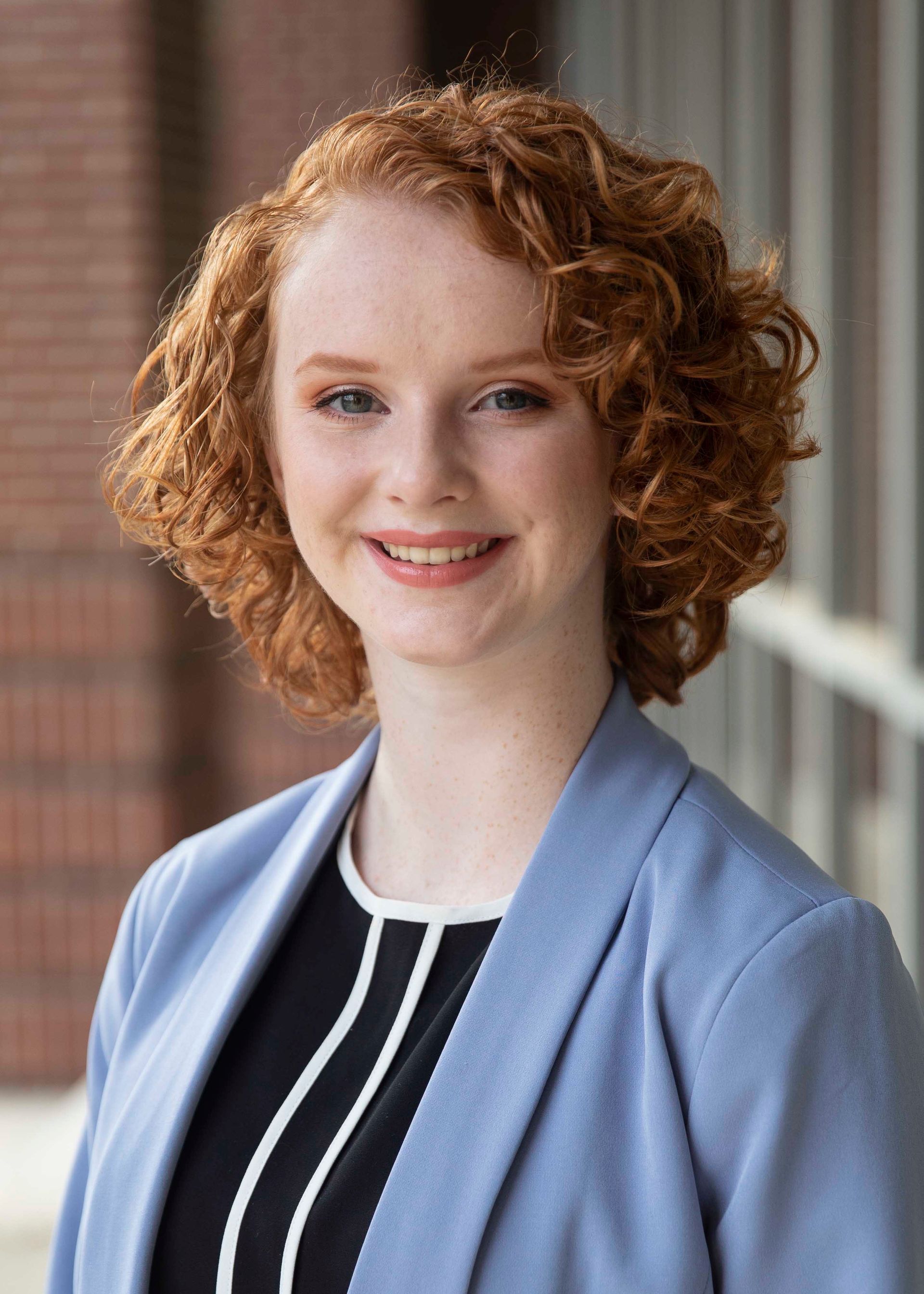 A woman with red hair is wearing a blue jacket and smiling for the camera.