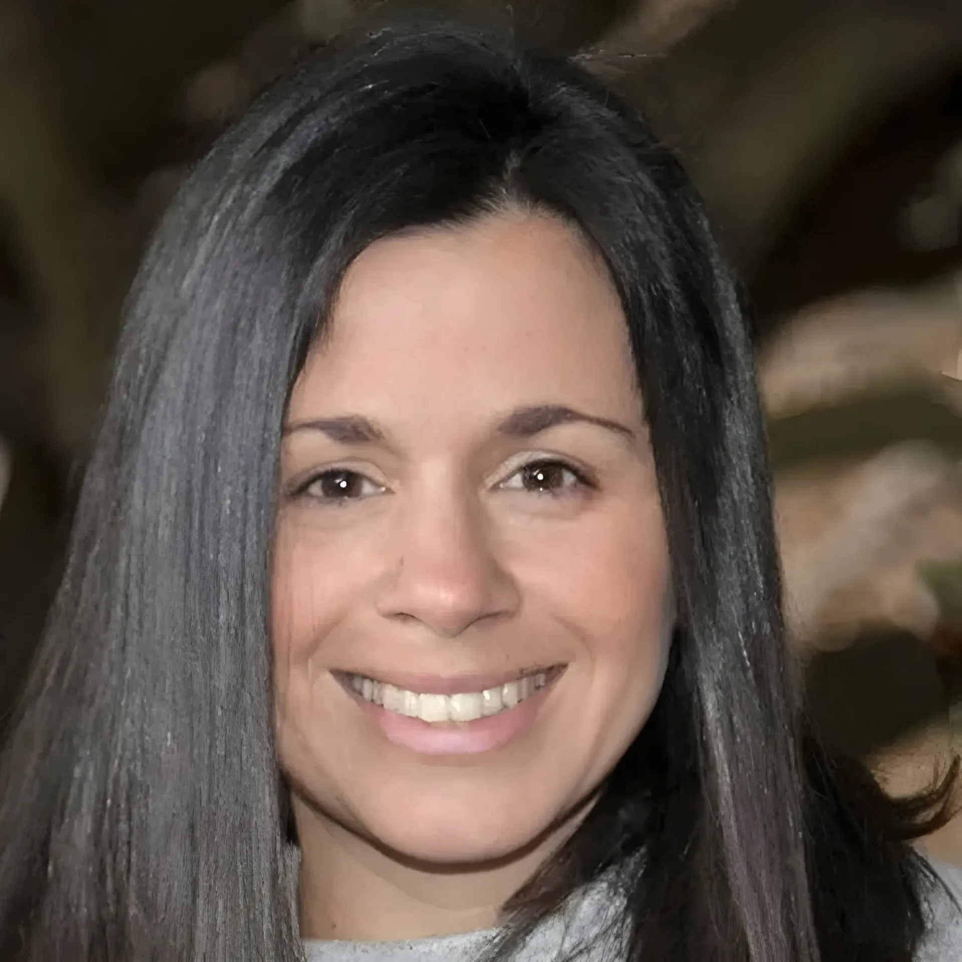A smiling person with long dark hair, facing forward against a soft-focus background.