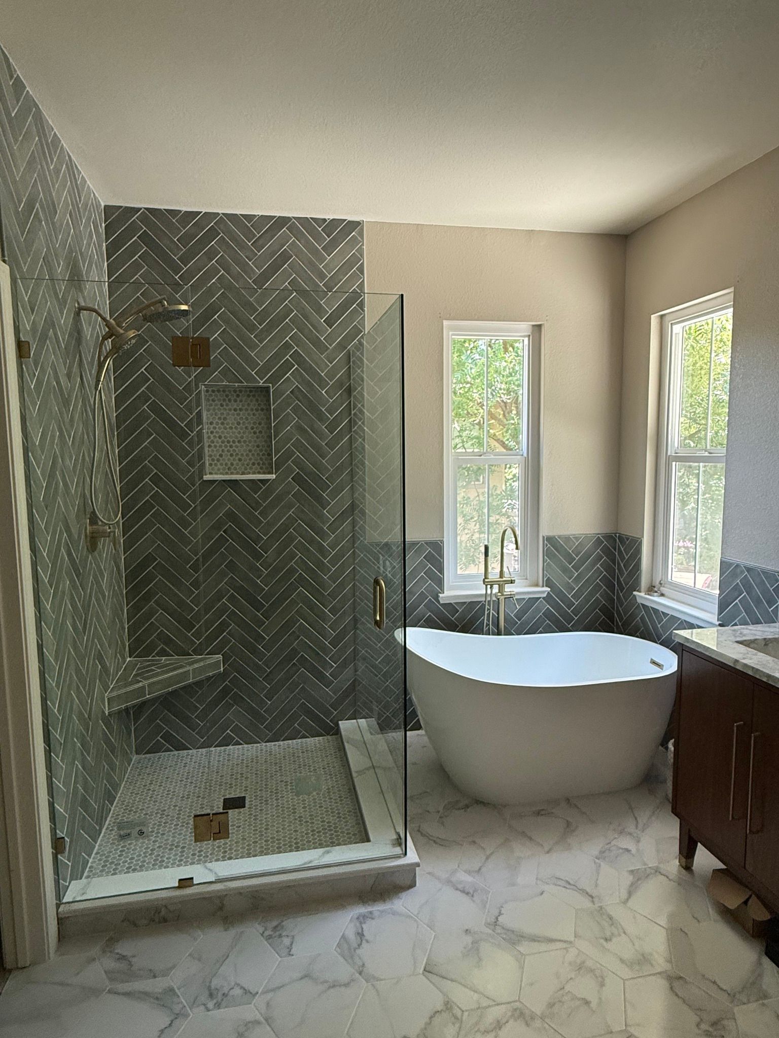 Modern bathroom with gray herringbone tile shower, freestanding tub, and marble flooring.