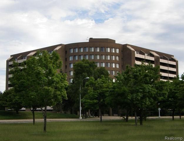 A large brown building is surrounded by trees and grass