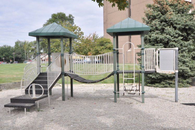 A playground set in a park with a building in the background.