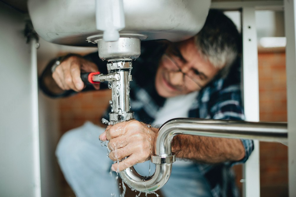 a man is fixing a sink pipe with water coming out of it