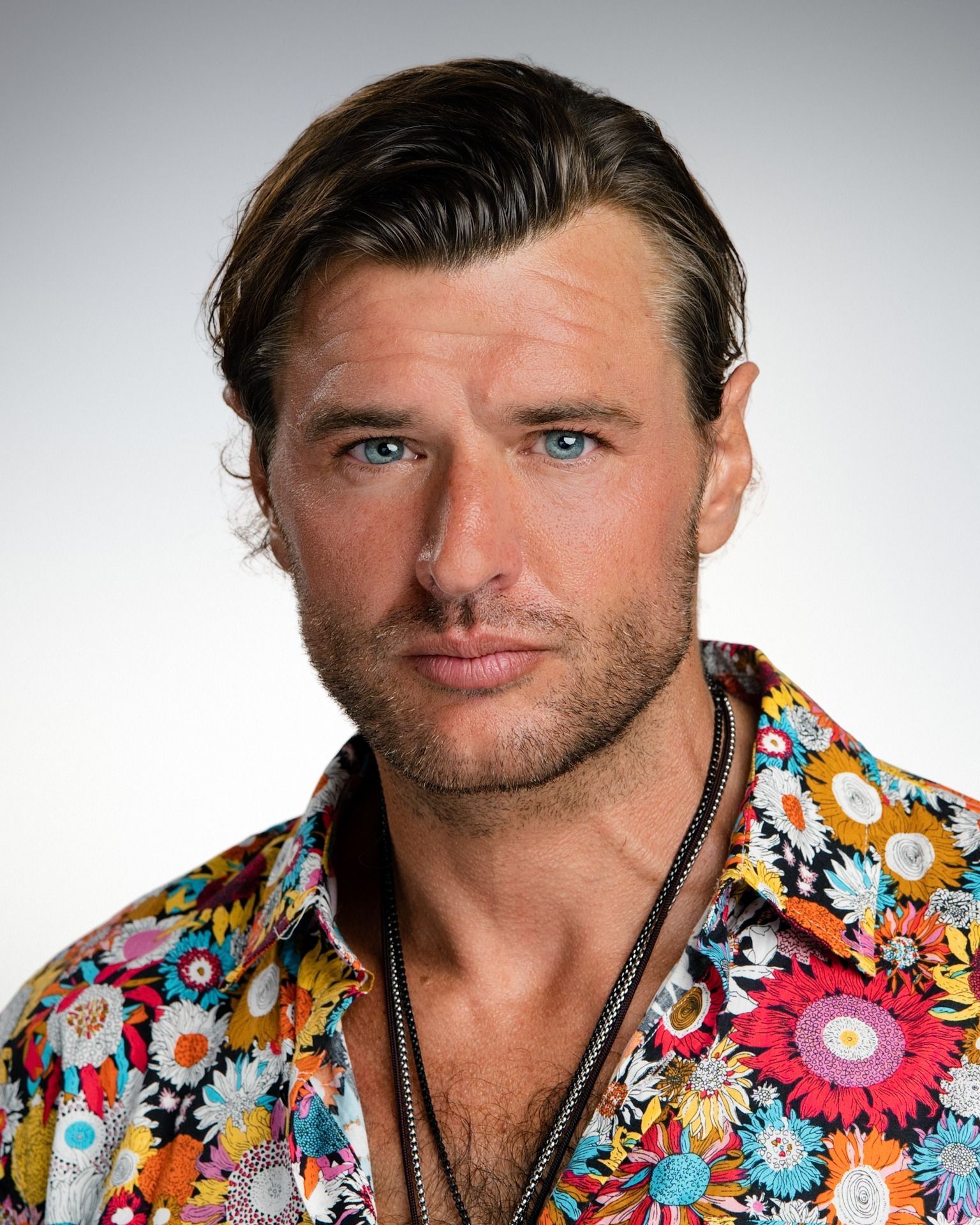 Man with blue eyes and short brown hair, wearing a colorful floral shirt.